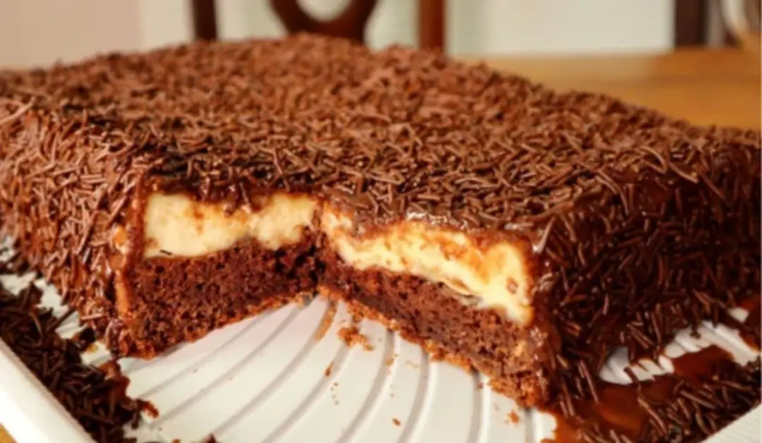 Bolo bomba de chocolate saindo recheado do forno, combinando massa fofinha com creme branco e cobertura. É uma opção pr…
